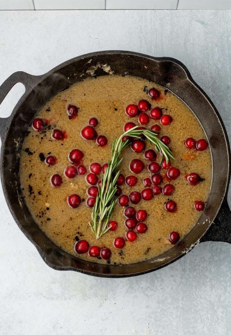ast-iron skillet filled with simmering sauce, fresh cranberries, and a sprig of rosemary, creating a fragrant maple cranberry glaze.