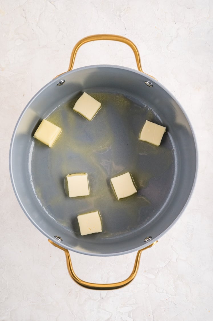 Cubed butter melting in a large pot to make Rice Krispie treats with marshmallow fluff.