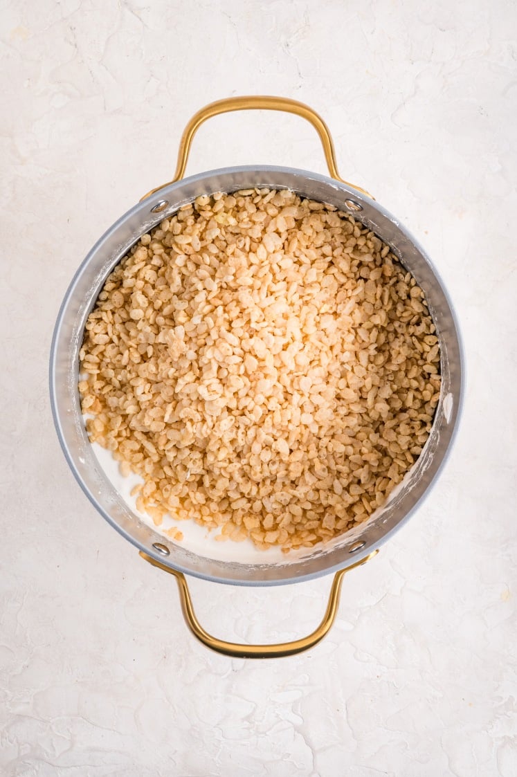 Rice cereal poured into melted marshmallow mixture in a pot.