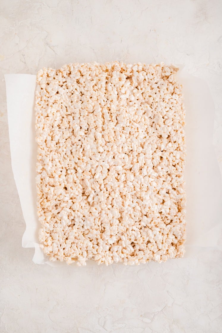 Rice Krispie treat mixture pressed into a parchment-lined baking dish.