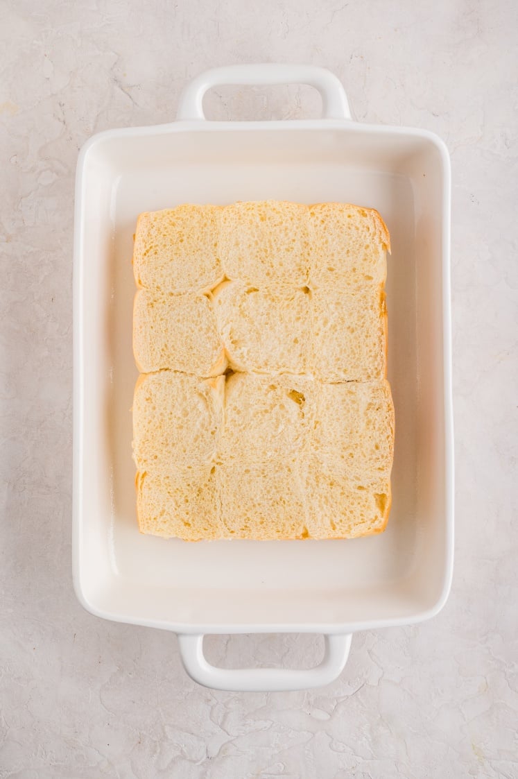 Top view of a white rectangular baking dish filled with a single layer of soft, square bread rolls placed closely together.