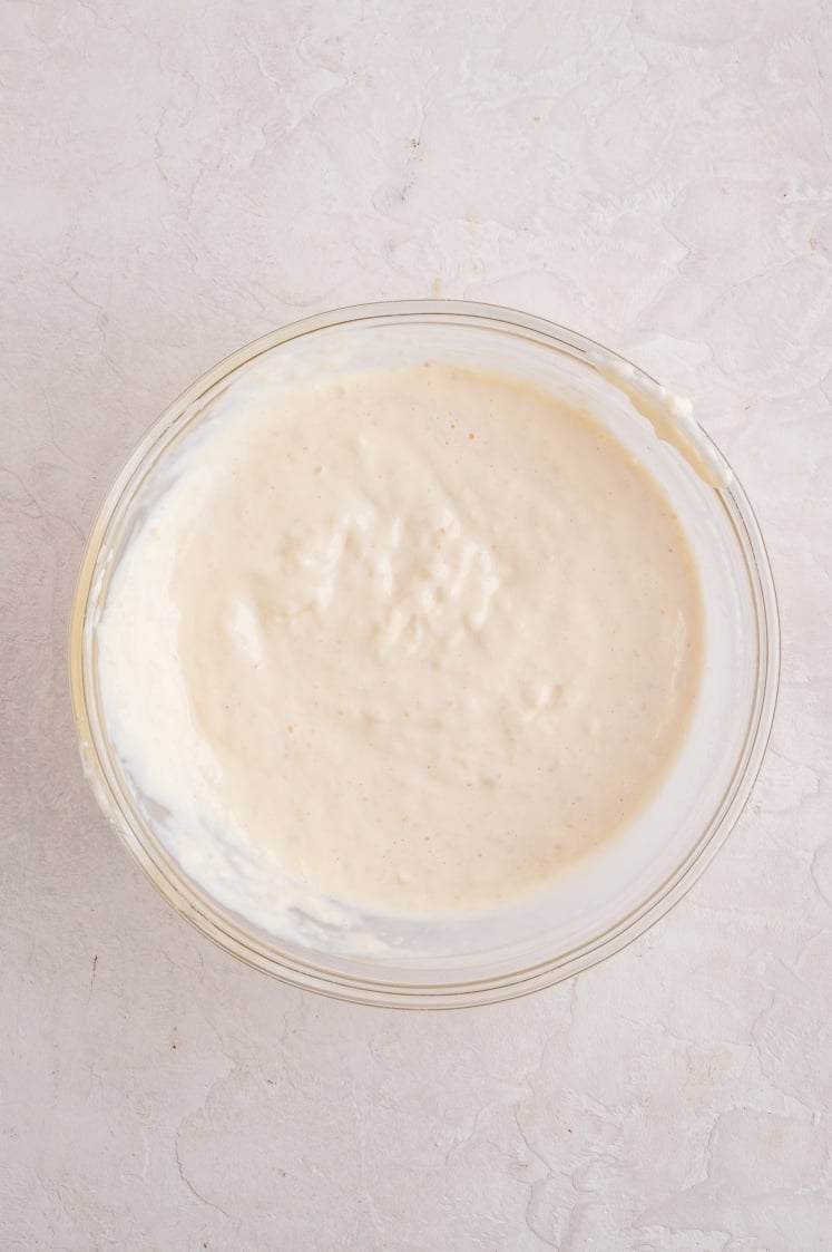 Top view of a glass bowl filled with a smooth, pale creamy mixture spread evenly across the bottom.