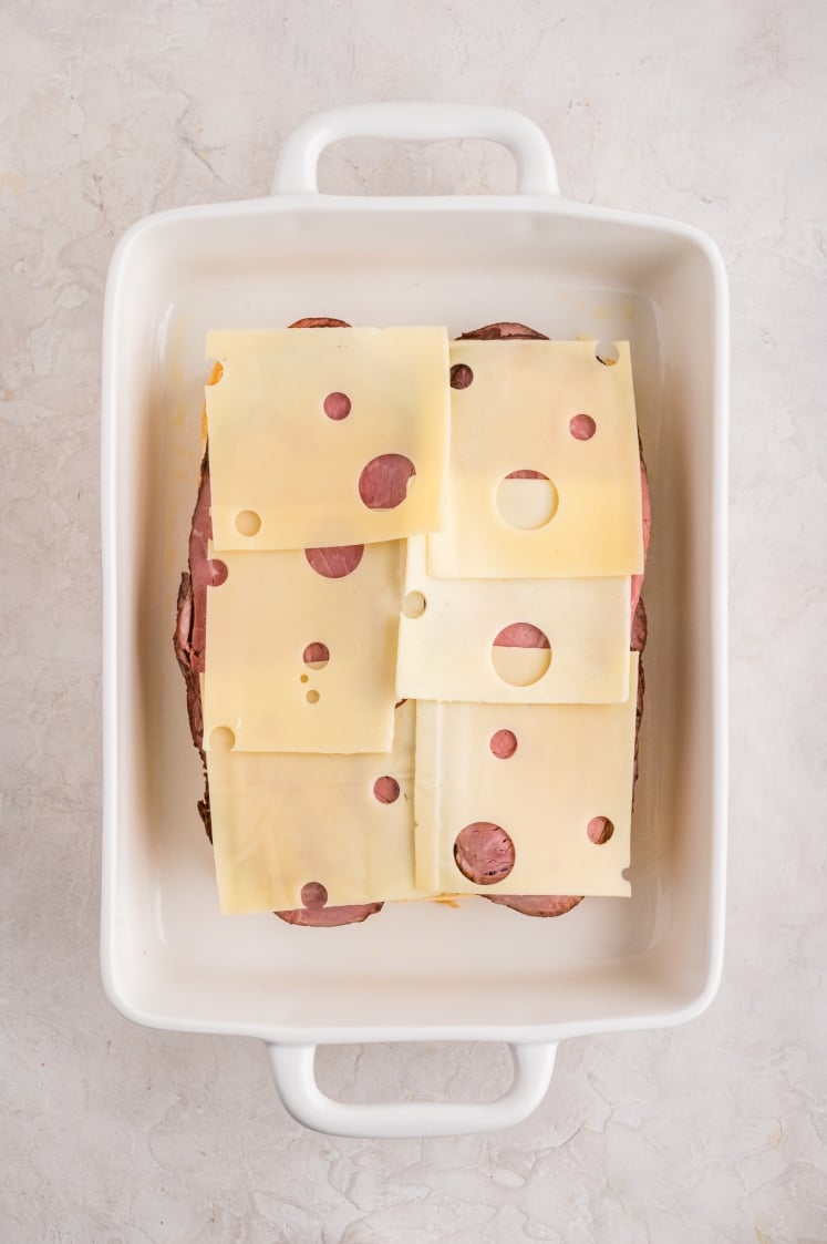 White baking dish with several slices of Swiss cheese layered over the roast beef