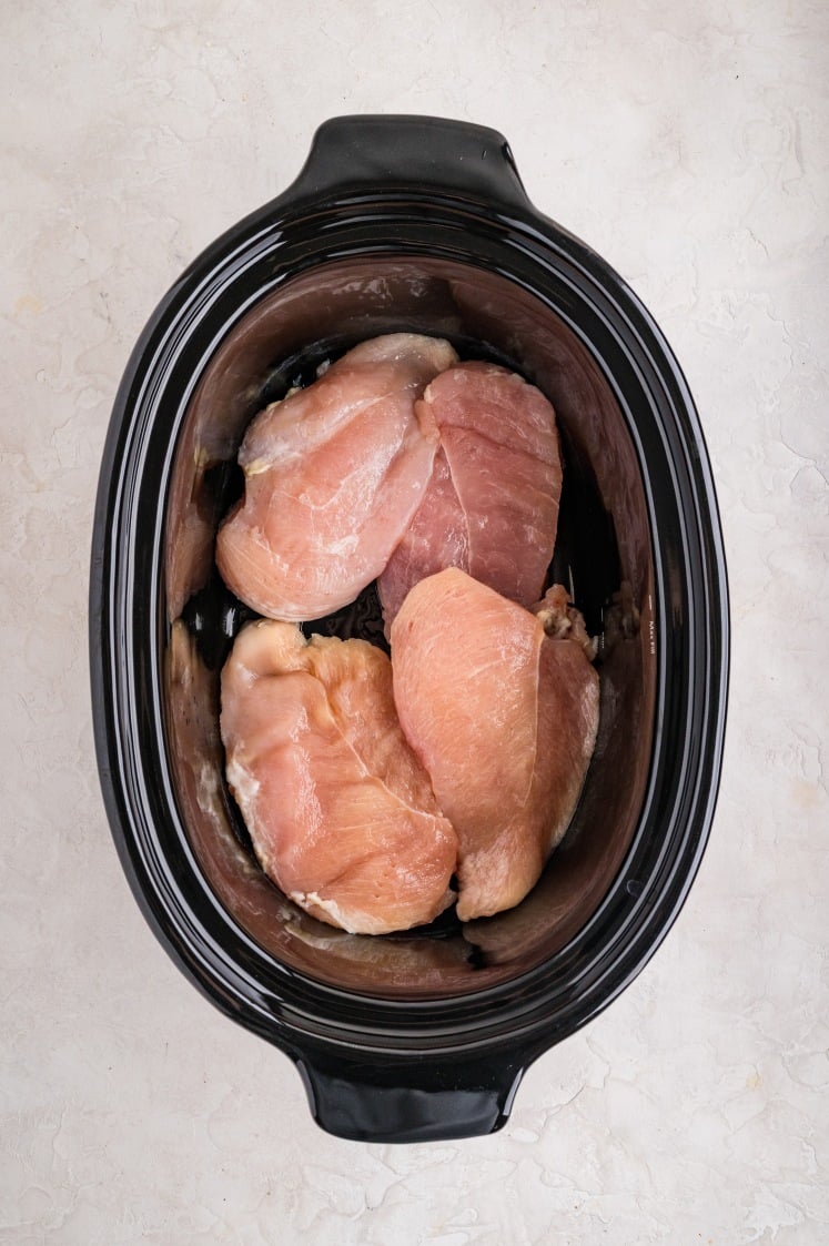 Raw chicken breasts placed inside a black slow cooker before cooking.