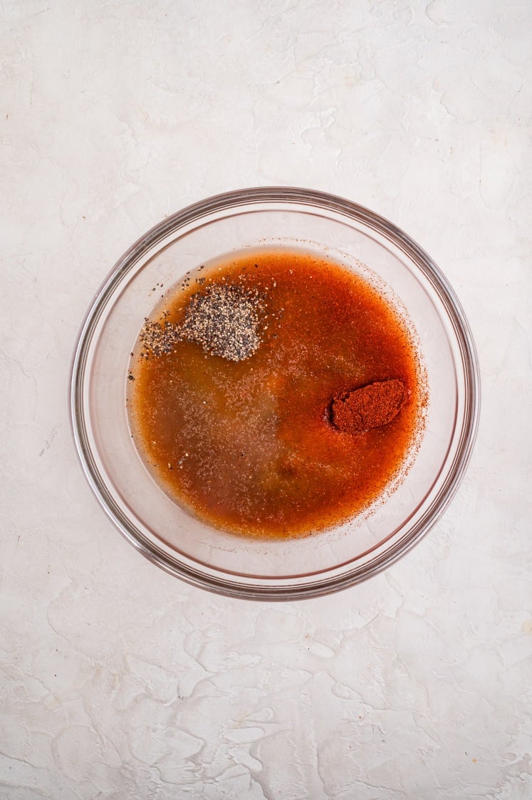 Glass bowl filled with chicken broth, spices, and seasoning mixtures before stirring.