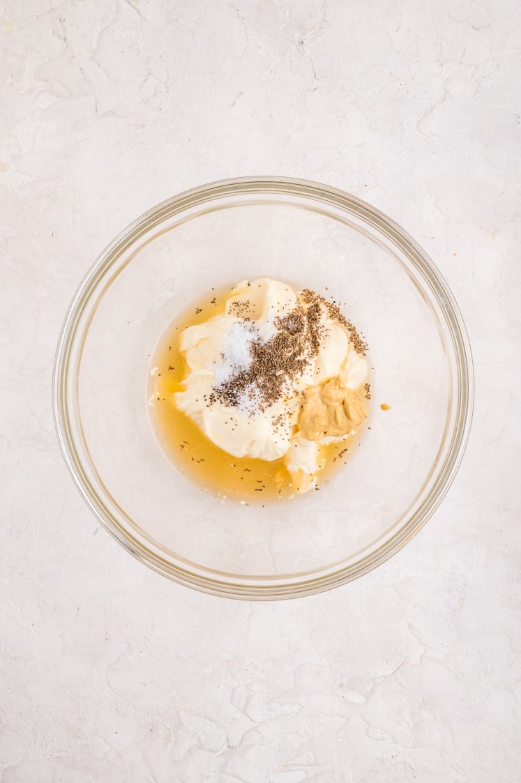 Glass bowl with mayonnaise, Dijon mustard, apple cider vinegar, salt, and pepper before mixing for coleslaw dressing.
