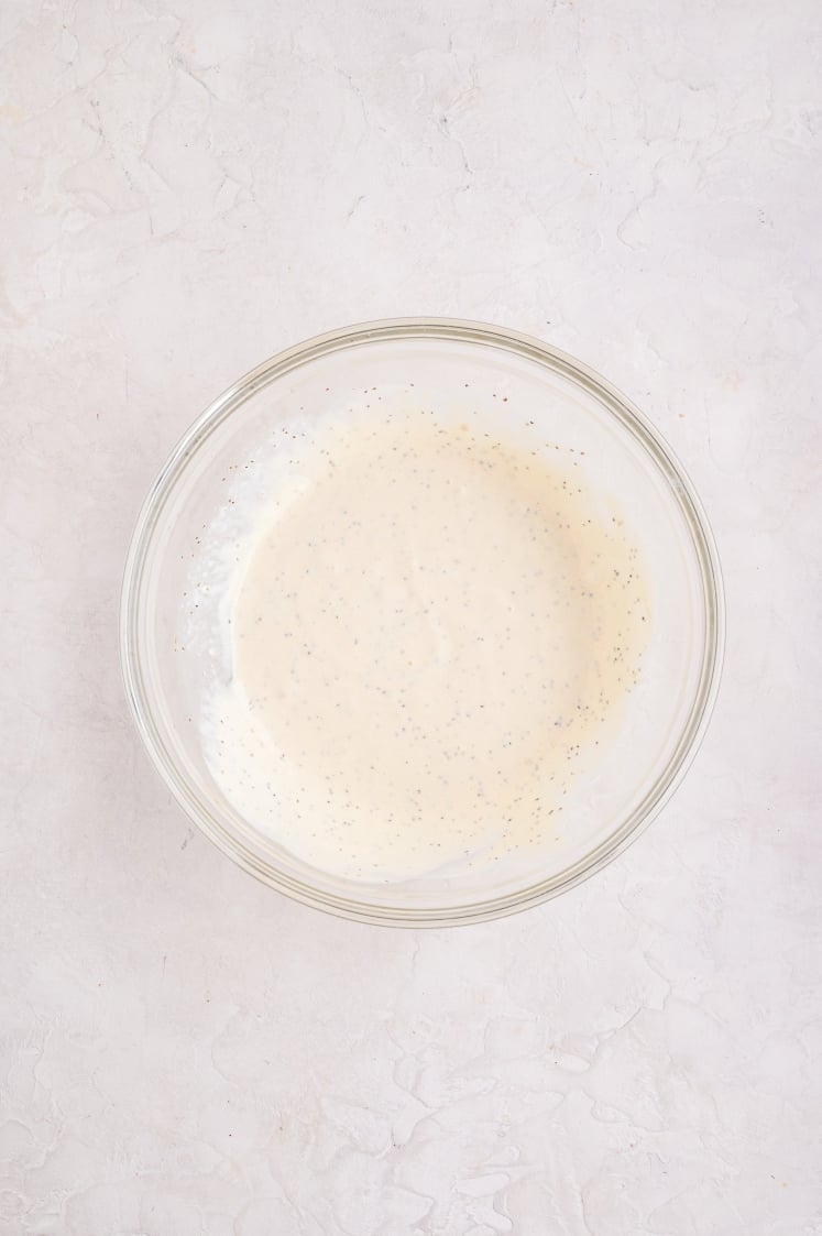 Glass bowl filled with creamy coleslaw dressing after mixing, with visible black pepper specks.
