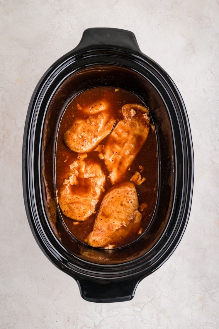 Cooked chicken breasts sitting in barbecue sauce inside a slow cooker after simmering.