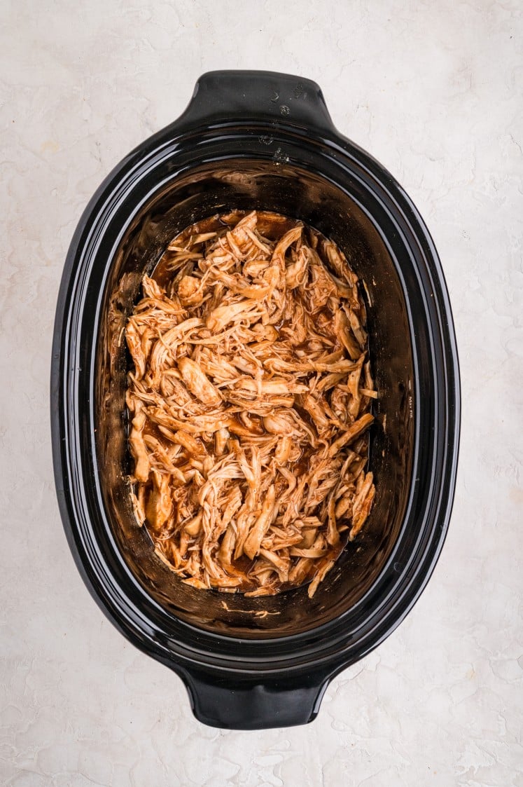 Shredded barbecue chicken inside a slow cooker after cooking, coated in sauce and ready to serve.