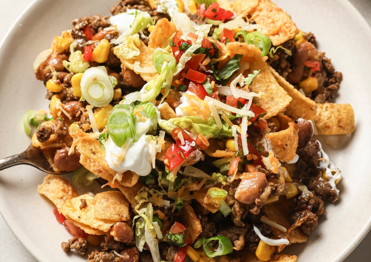 A casserole dish of walking taco bake topped with toppings.