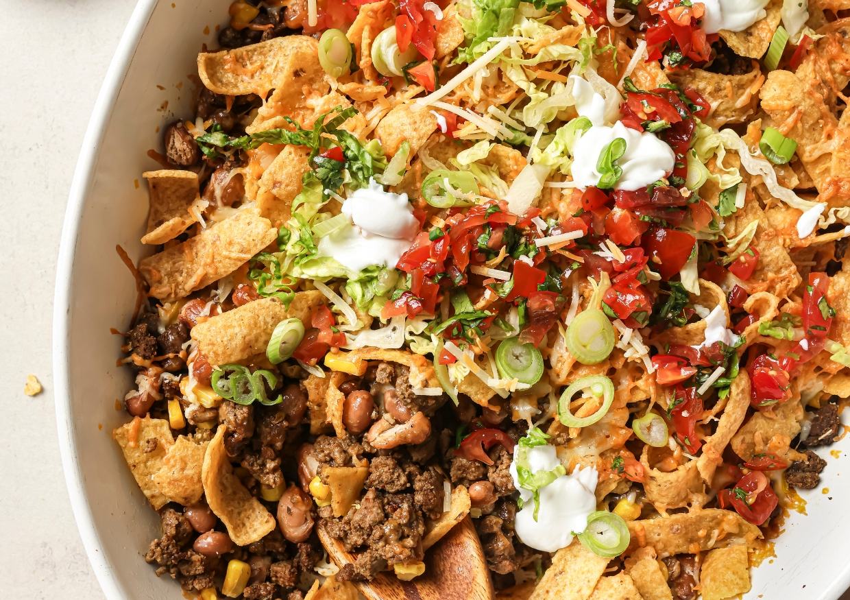 A casserole dish of walking taco bake topped with toppings.