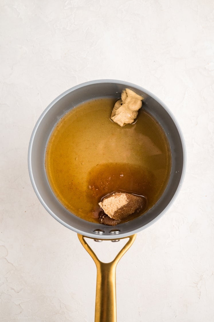 Sauce ingredients for bacon wrapped pork tenderloin, including mustard, brown sugar, and maple syrup, heating in a saucepan.