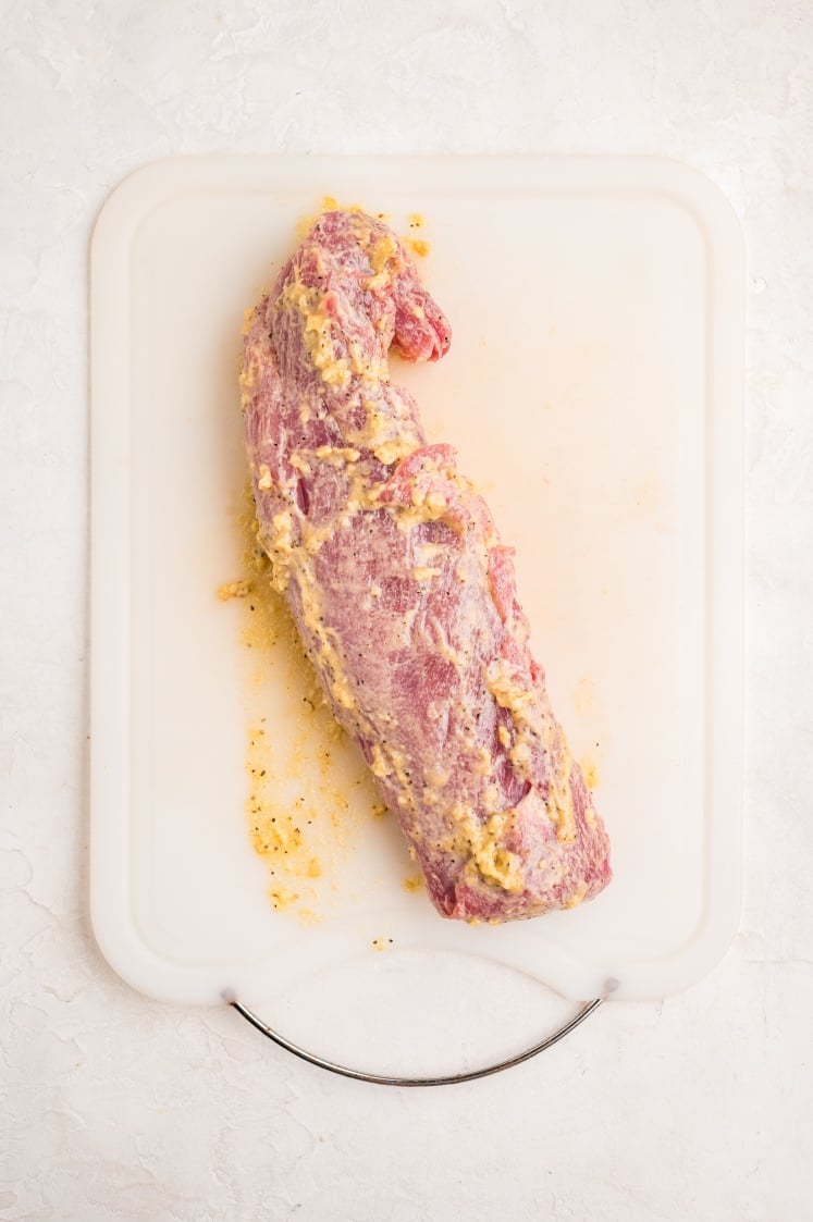 Raw pork tenderloin coated with garlic mustard seasoning before wrapping with bacon.