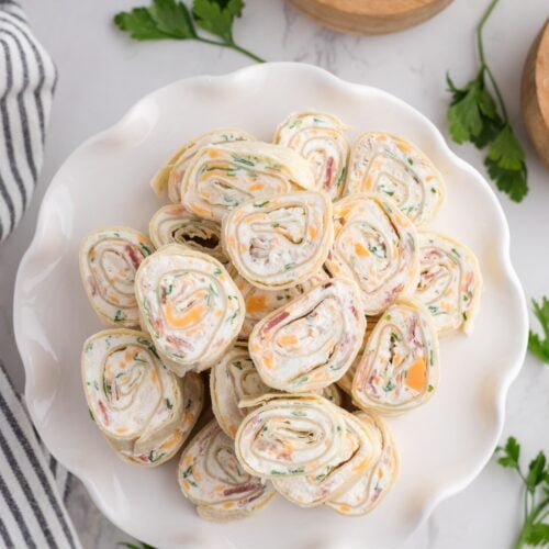 Plate of crack chicken pinwheels filled with creamy chicken, cheddar, bacon, and green onions, served on a white dish.