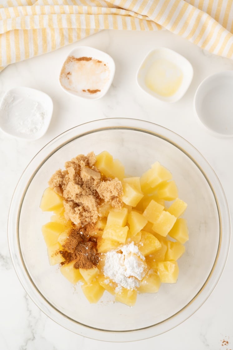 Glass bowl with pineapple and seasoning ingredients.