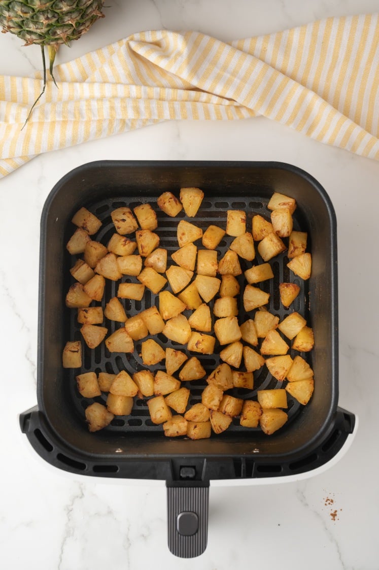 “Cooked pineapple pieces in an air fryer basket.