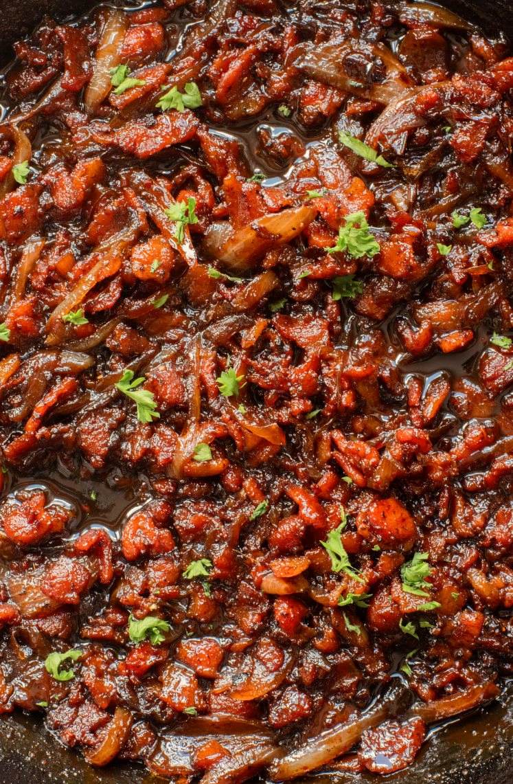 Close-up of caramelized onions and tomatoes cooked with spices and garnished with fresh parsley in a pan.