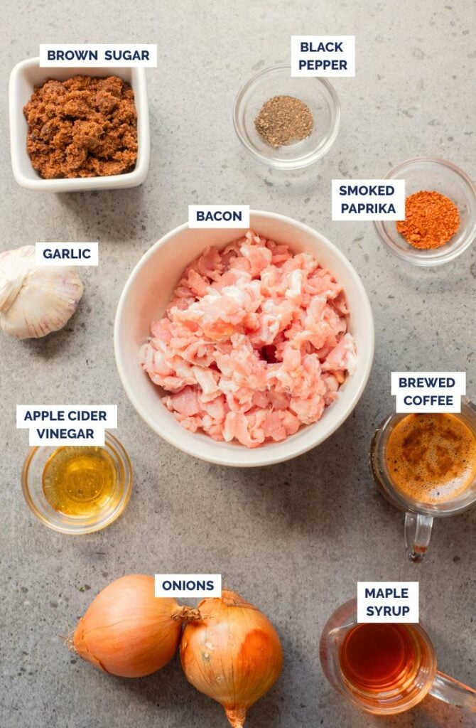 Ingredients for a recipe arranged on a countertop: chopped bacon, brown sugar, black pepper, smoked paprika, brewed coffee, maple syrup, garlic, onions, and apple cider vinegar.