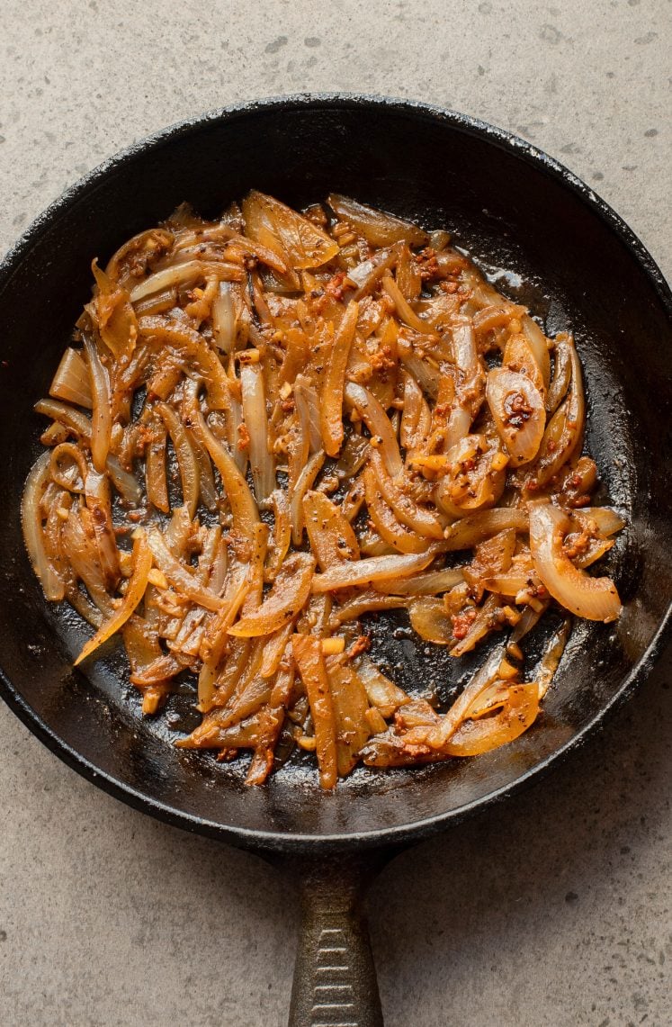A cast iron skillet with sautéed onions and garlic on a light gray surface.
