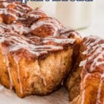 A loaf of cinnamon pull-apart bread with icing drizzle is partially sliced on a white surface, with a bottle of milk in the background.