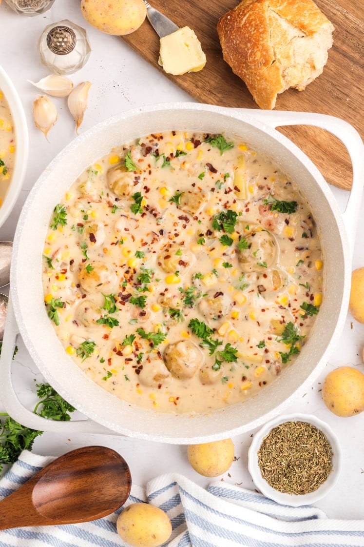 Pot of creamy corn and potato chowder garnished with parsley and red pepper flakes.
