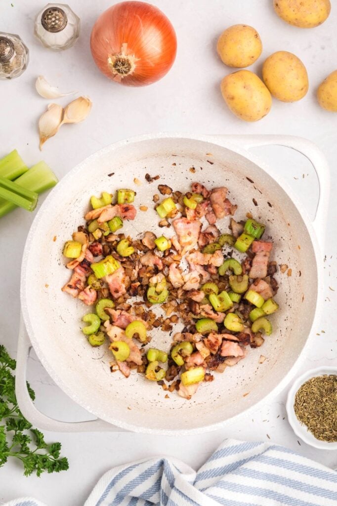 Bacon and celery cooking together in a pot until browned.
