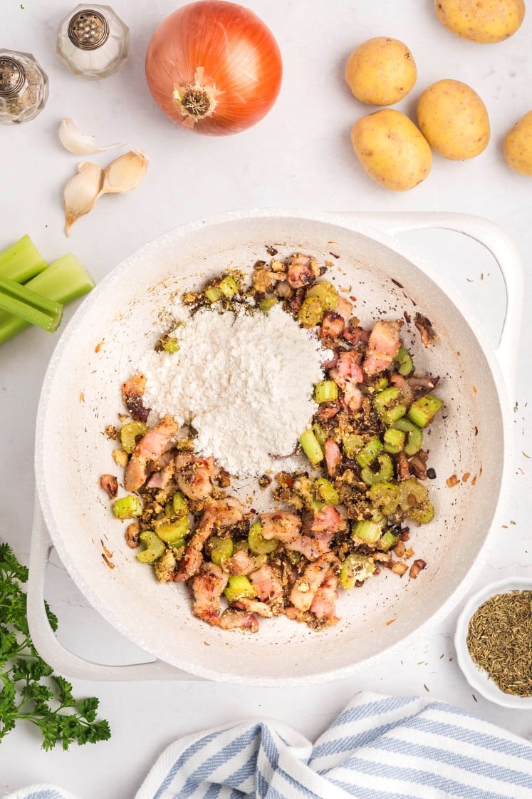 Flour added to seasoned bacon and celery in a pot.
