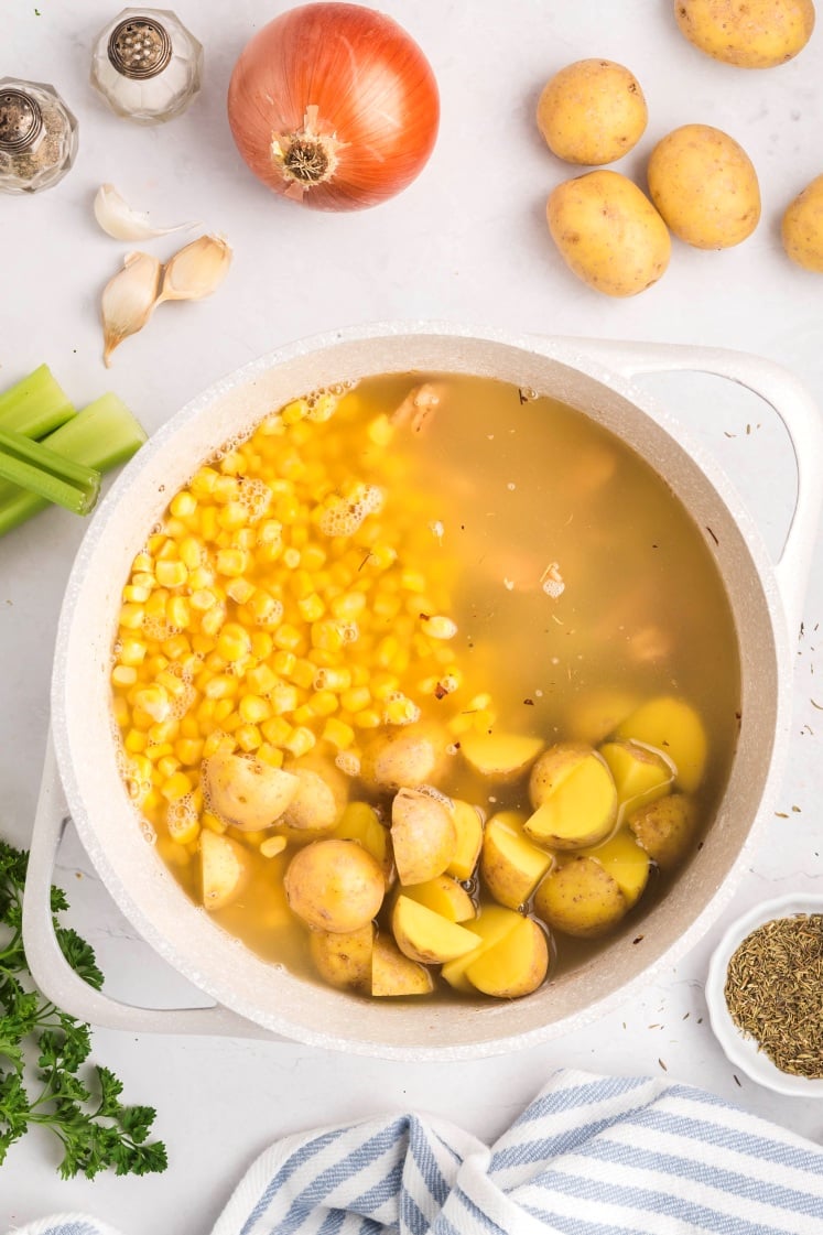 Corn and potatoes simmering in broth in a pot.