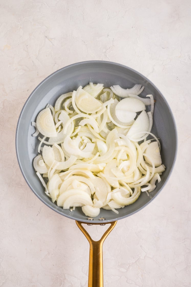 Skillet filled with sliced onions cooking in oil.