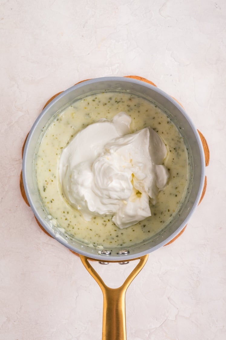 Thick creamy sauce in a saucepan with a large dollop of sour cream on top.