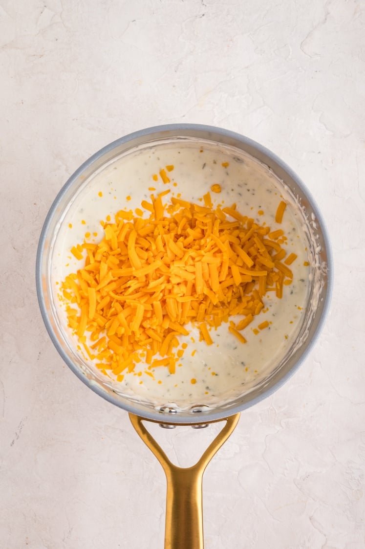 Shredded cheddar cheese added to a pot of creamy sauce.