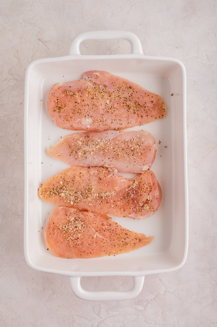 Seasoned raw chicken breasts arranged in a white baking dish.
