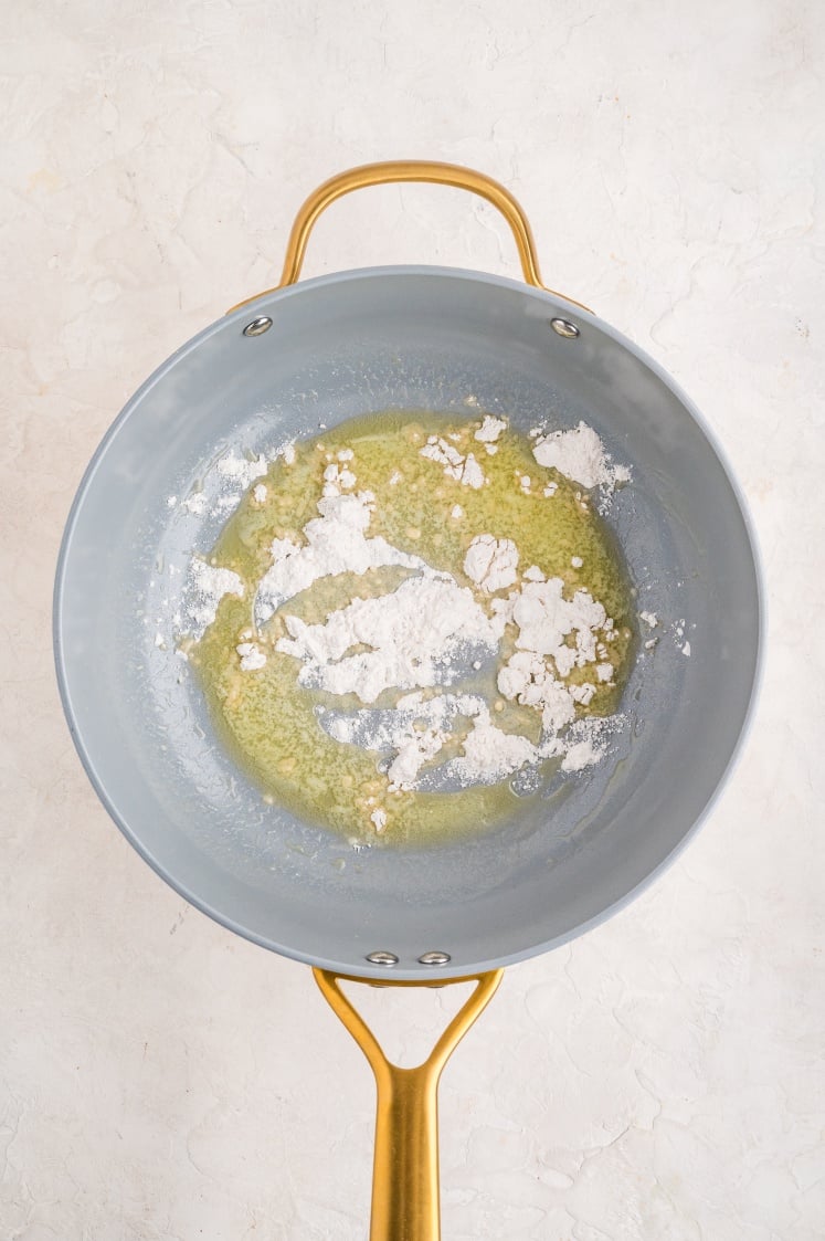 Overhead view of flour mixed into melted butter in a pan.
