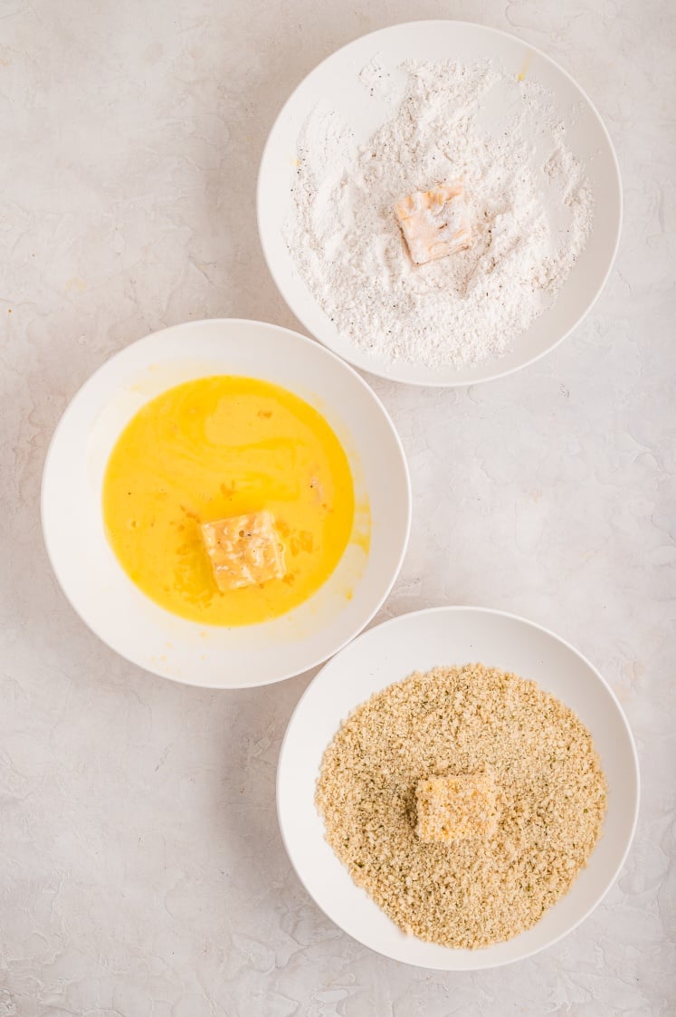 Mac and cheese bites being coated in flour, egg wash, and breadcrumbs.
