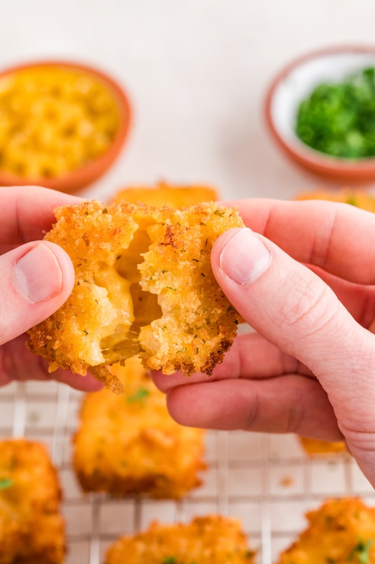 Hands pulling apart a fried mac and cheese bite to show the melted cheese inside.