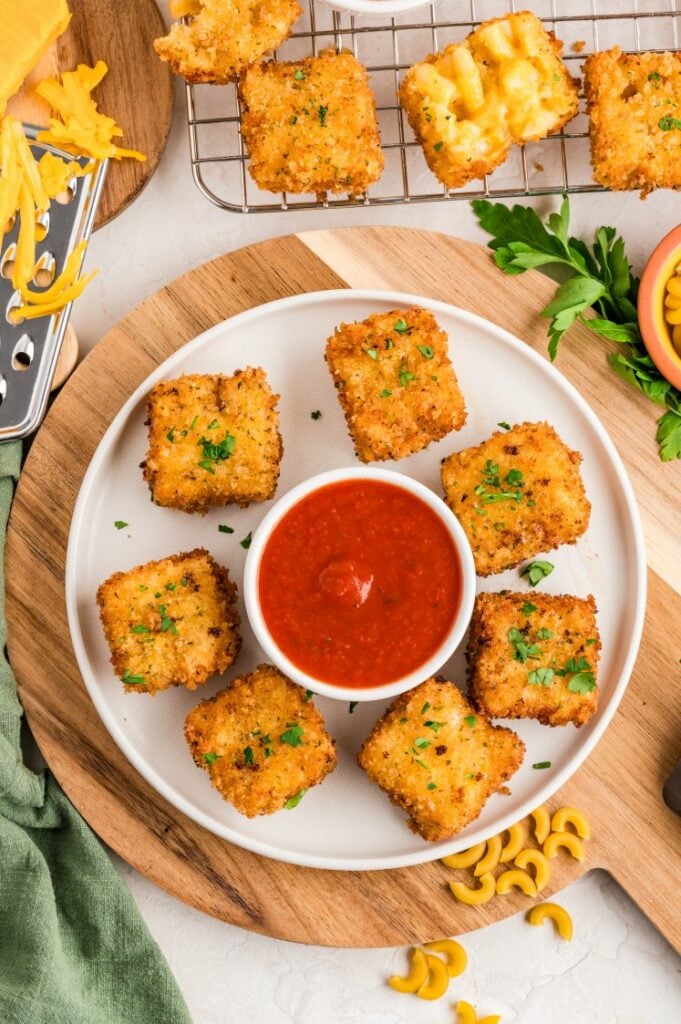 Fried mac and cheese bites arranged around a bowl of marinara sauce on a white plate.