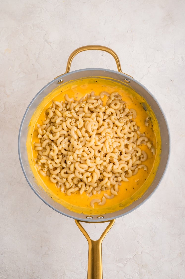 Cooked elbow macaroni added to cheese sauce in a saucepan.