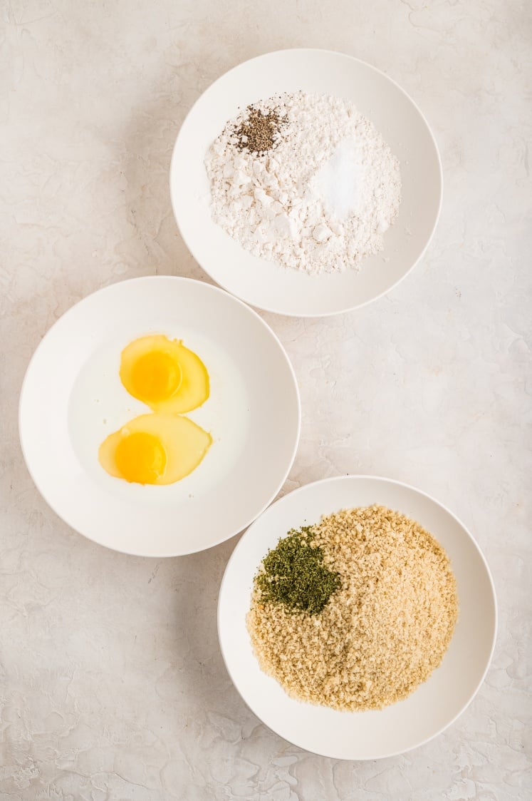 "Plates of flour, beaten eggs, and seasoned breadcrumbs arranged for breading.
