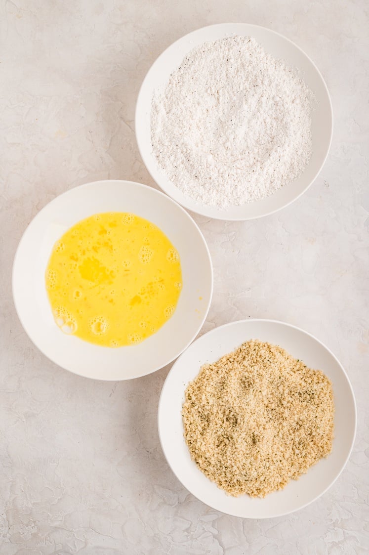 Three bowls with flour, beaten eggs, and breadcrumbs arranged for breading.