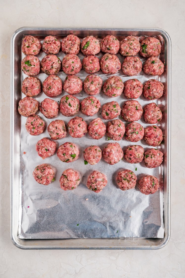 Raw meatballs rolled and placed on a baking sheet.