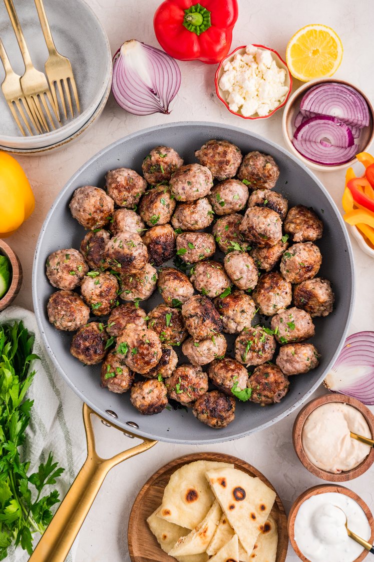 Fully cooked Greek meatballs in a skillet with fresh herbs.