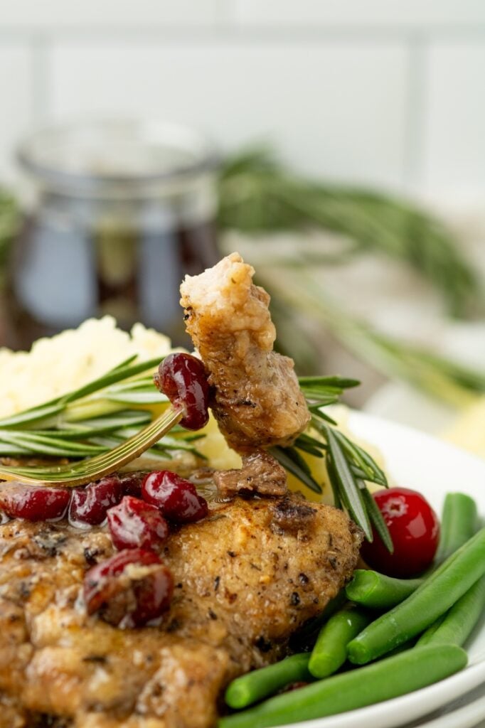 A plate of breaded chicken garnished with cranberries and rosemary, served with green beans and mashed potatoes.