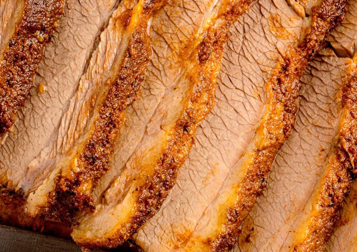 Close-up of several slices of cooked, seasoned beef brisket, showing the texture and seasoning on the meat.