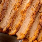 Sliced cooked brisket arranged on a wooden cutting board with a knife partially visible underneath.