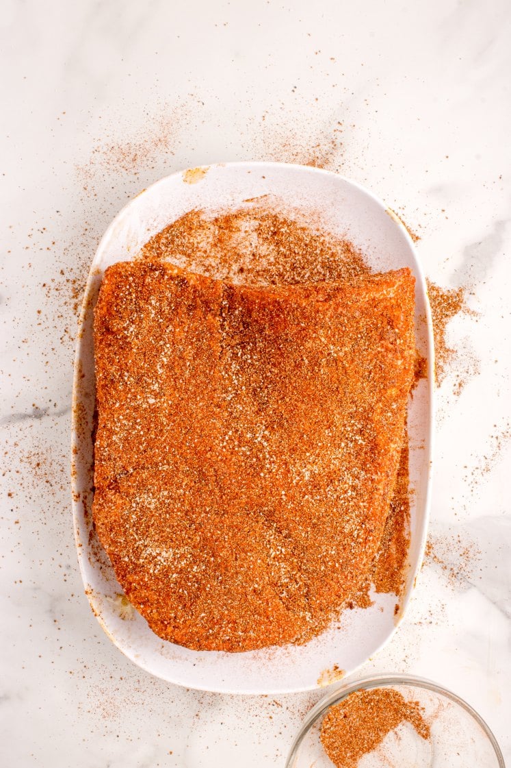 Raw oven-baked brisket on a white platter coated in a generous layer of dry rub seasoning.