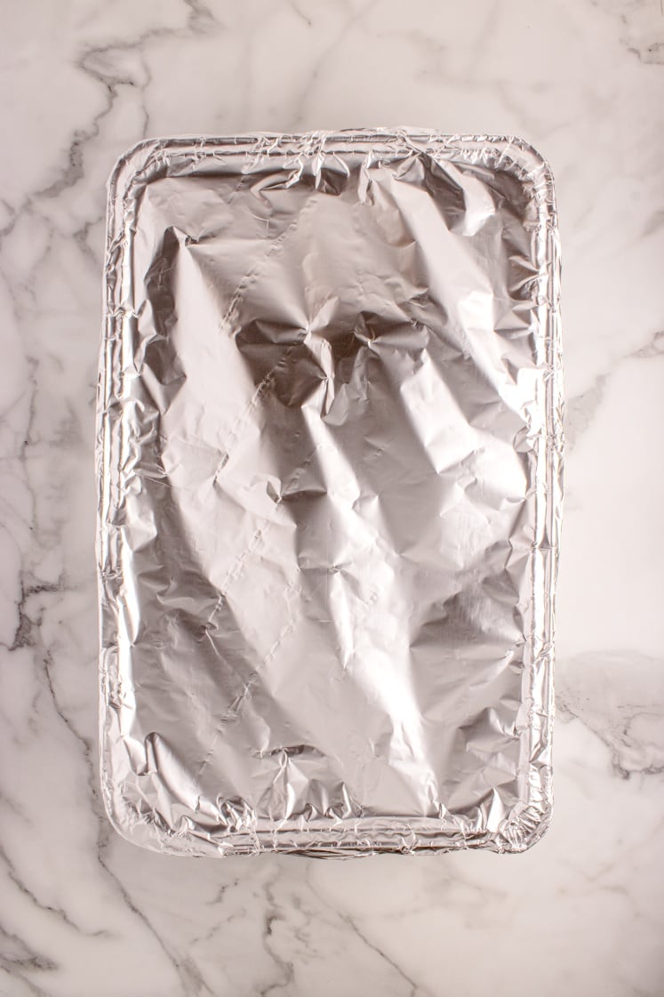 Foil-covered roasting pan on a marble surface, sealed tightly for slow cooking.