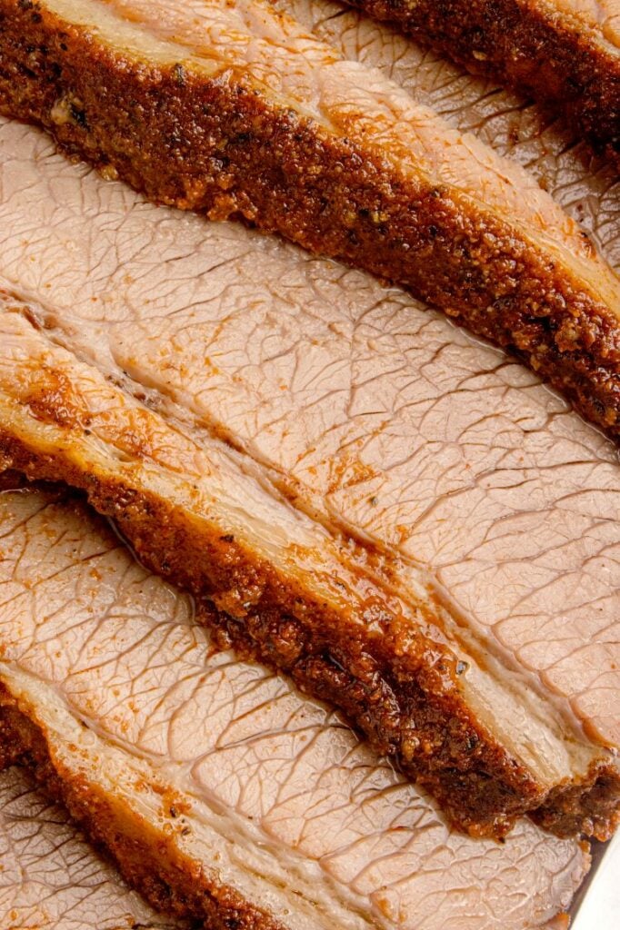 Close-up of several slices of cooked beef brisket, showing a seasoned crust and juicy, tender meat.