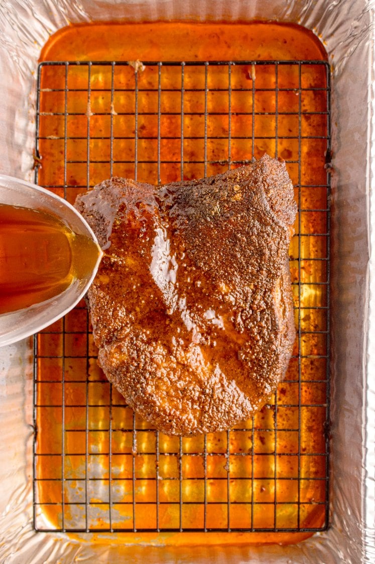 Cooked oven-baked brisket on a wire rack while pan juices are being poured over the top for basting.