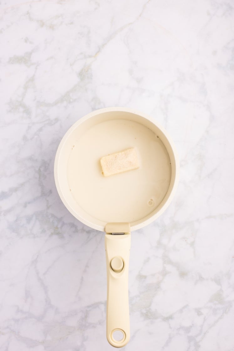 Saucepan filled with warm milk and a piece of butter beginning to melt.