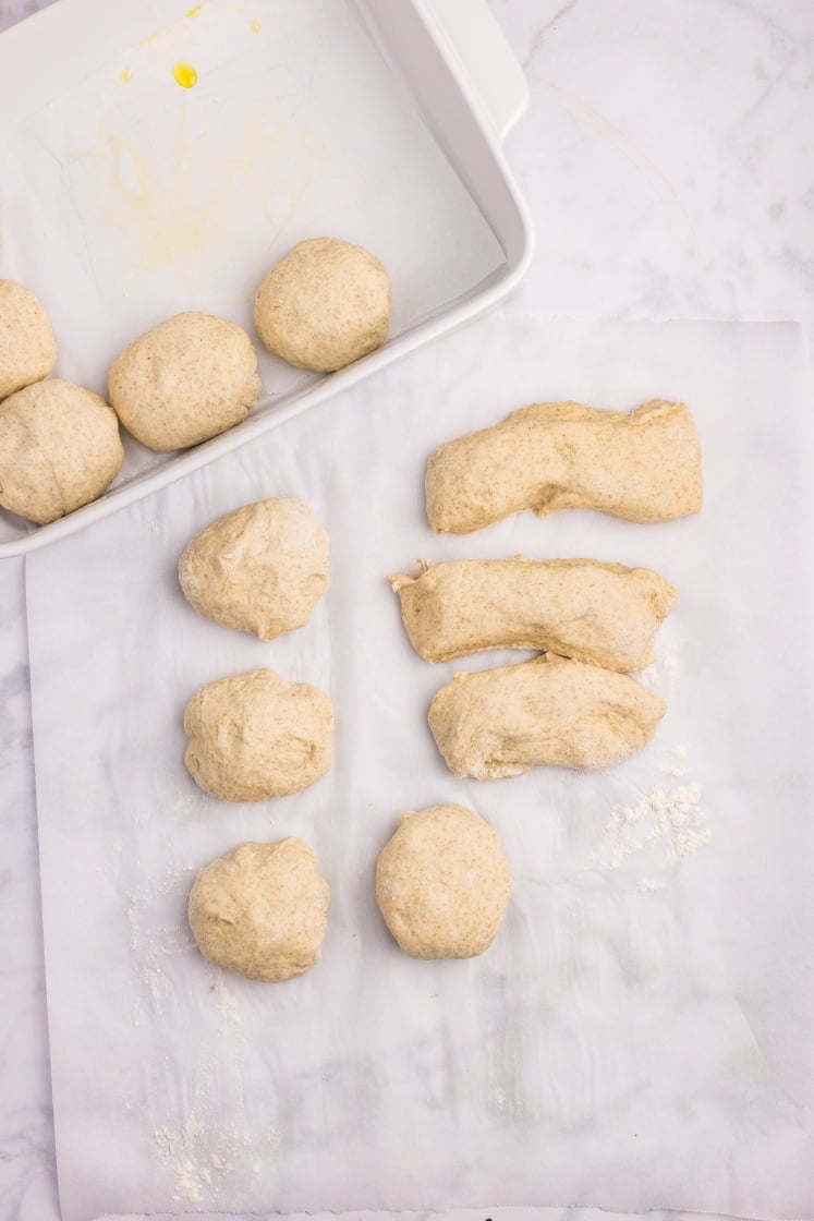 Shaped dough balls arranged on parchment paper and placed into a baking dish.